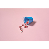 Pharmaceutical capsules falling out of bucket over pink background. Flat lay with copy space. Health care and medication-assisted treatment.