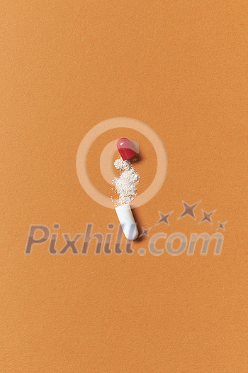 Pharmaceutical tablet open with medication powder scattered over orange background. Health care and medication-assisted treatment. Pharmaceutical tablet open with medication powder scattered over orange background. Health care and medication-assisted treatment.