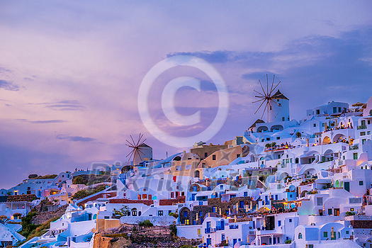 Famous greek iconic picturesque tourist destination Oia village with traditional white houses and windmills in Santorini island in evening dusk, Greece Famous greek iconic picturesque tourist destination Oia village with traditional white houses and windmills in Santorini island in evening dusk, Greece