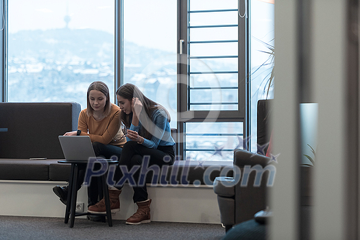 Two businesswomen sitting in a modern coworking space on a break from work and relaxing using a laptop. Selective focus. High-quality photo Two businesswomen sitting in a modern coworking space on a break from work and relaxing using a laptop. Selective focus. High-quality photo