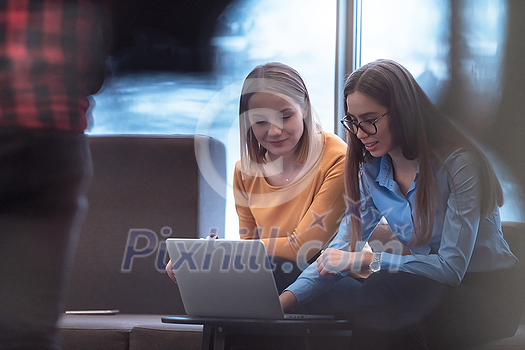 Two businesswomen sitting in a modern coworking space on a break from work and relaxing using a laptop. Selective focus. High-quality photo Two businesswomen sitting in a modern coworking space on a break from work and relaxing using a laptop. Selective focus. High-quality photo