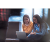 Two businesswomen sitting in a modern coworking space on a break from work and relaxing using a laptop. Selective focus. High-quality photo