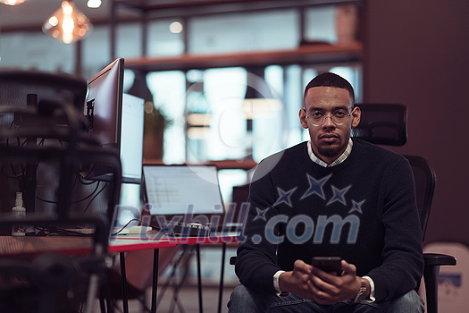 Young African American work in coworking space using smartphones analyzing online market trends, focused man worker reading financial news or browsing the internet on phone. Technology concept. High-quality photo