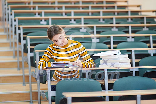 Female student taking notes from a book at school calssroom. Young woman sitting at table doing assignments Female student taking notes from a book at school calssroom. Young woman sitting at table doing assignments