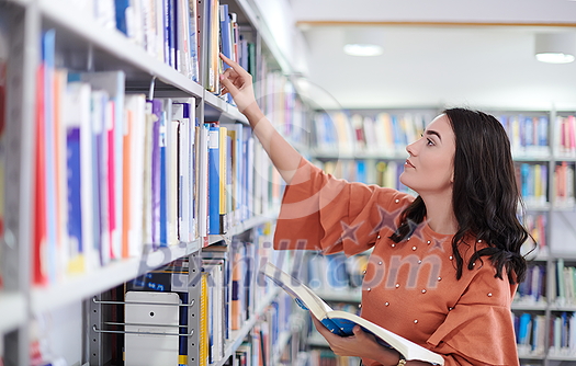 Reading a book in library. Young attractive librarian reading a book between library bookshelves Reading a book in library. Young attractive librarian reading a book between library bookshelves