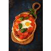 Homemade tasty pizza with egg, cheese, tomatoes and basil on dark background. Top view.