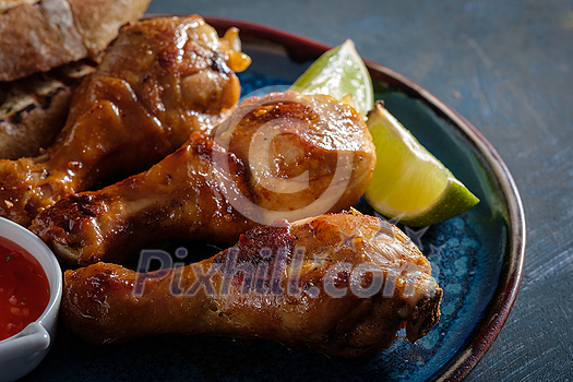 Fried spicy chicken legs in a ceramic dish with red sauce and lime. Fried spicy chicken legs in a ceramic dish with red sauce and lime.