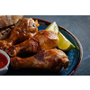 Fried spicy chicken legs in a ceramic dish with red sauce and lime.