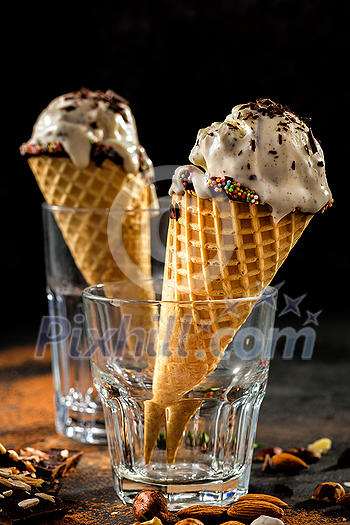 Creamy ice cream with chocolate crumbs in a waffle cone stands in a glass over dark background Creamy ice cream with chocolate crumbs in a waffle cone stands in a glass over dark background