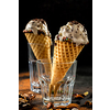 Creamy ice cream with chocolate crumbs in a waffle cone stands in a glass over dark background