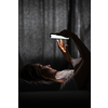 Young woman in bed holding a phone, tired and exhausted, blue light straining her eyes, messing up her circadian rhytm