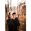 Young woman with binoculars outdoors on fall day. Enjoying the outdoors.