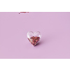 Red dried aroma rose petals inside small transparent heart-shaped pendant on toned background, close up with copy space. Creative wedding invitation card design.