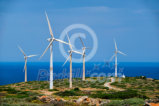 Green renewable alternative energy concept - wind generator turbines generating electricity. Wind farm on Crete island, Greece with small white church Green renewable alternative energy concept - wind generator turbines generating electricity. Wind farm on Crete island, Greece with small white church
