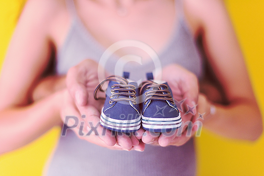 young pregnant couple holding newborn baby shoes isolated on yellow background,family and parenthood concept young pregnant couple holding newborn baby shoes isolated on yellow background,family and parenthood concept