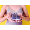young  pregnant couple holding newborn baby shoes isolated on yellow background,family and parenthood concept