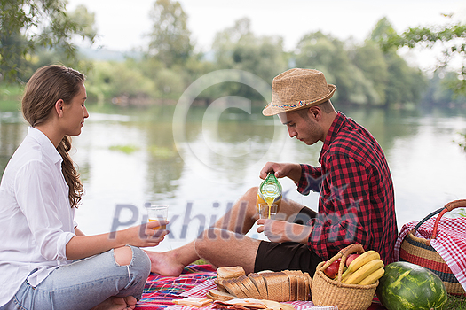 Couple in love enjoying picnic time drink and food in beautiful nature on the river bank Couple in love enjoying picnic time drink and food in beautiful nature on the river bank