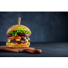 Tasty grilled beef burger with lettuce, cheese and onion served on cutting board on a black wooden table, with copyspace