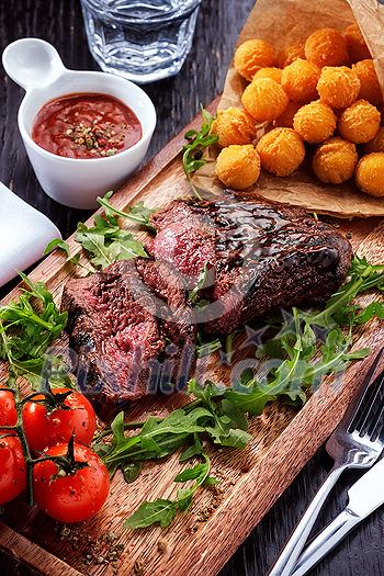 Juicy rare sliced grilled fillet steak served with tomatoes and cheese balls on an old wooden board. Top view. Juicy rare sliced grilled fillet steak served with tomatoes and cheese balls on an old wooden board. Top view.